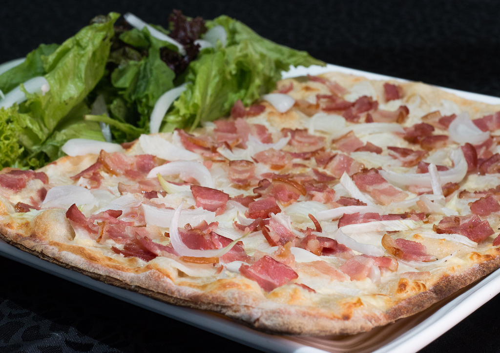 Flammekueche or "tarte flambée" comes from Alsace in Eastern France, on the German border. The thin crust pizza is topped with lardons (bacon strips), white onions and a cream-based sauce made with fromage blanc and crème fraiche.